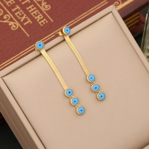 Détail de boucles d'oreilles pompon en chaîne serpent dorée avec breloques œil bleu sur cuir