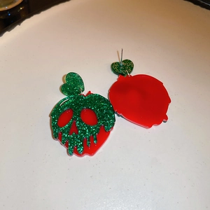 Macro detail of acrylic poison apple skull earrings with green glitter and red finish