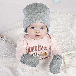 Detail of baby knit hat and glove set worn with a printed onesie on a soft knit blanket
