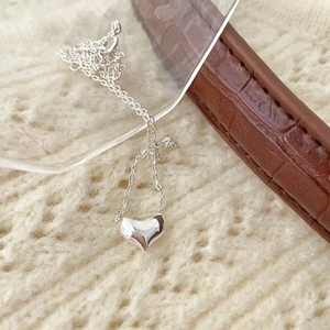 Detail shot of heart pendant on a fine silver chain over beige knit sweater