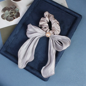 Close-up of a grey satin hair scrunchie with a large bow and pearl on a velvet tray