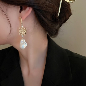 Detail of elegant gold woven knot earrings with large baroque pearls on model