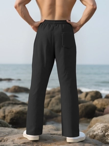 Detail of men's black pleated trousers with draped texture against a coastal backdrop