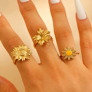 Detail of three-piece gold sunflower and maple leaf rings with yellow enamel on hand