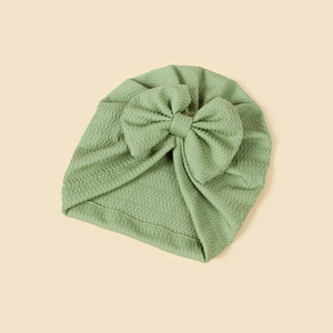 Close-up of green knitted baby turban hat with a large bow and ribbed texture