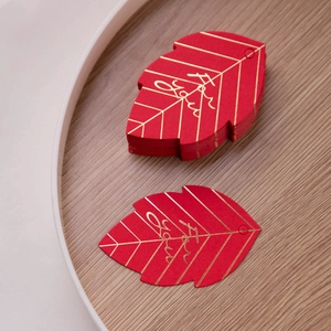 Macro shot of red leaf-shaped gift tags with gold foil veins in a wooden tray