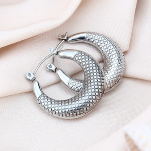 Detailed view of silver hoop earrings with textured grid patterns on soft fabric