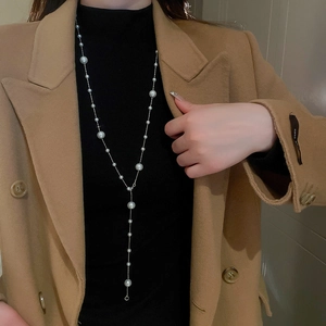 Silver Y-shaped necklace with irregular pearls shown on a model wearing a brown coat