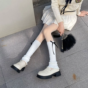 Close-up of white ribbed knit leg warmers with black satin bows and chunky loafers