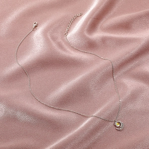 Detail of moon pendant necklace with iridescent stone on pink silk background