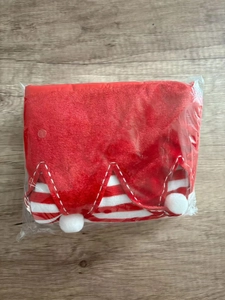 Detail of a red velvet Christmas stocking with striped trim and white pom poms in packaging