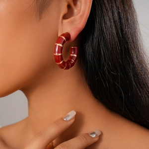 Close-up of a red round C-shape earring with golden stripes on a model's ear lobe