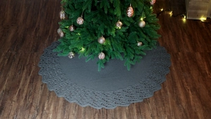 Close-up of grey knitted Christmas tree skirt with hollow wavy edges on dark wood floor