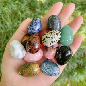 Close-up of hand holding various colorful 30mm natural gemstone egg-shaped stones on grass