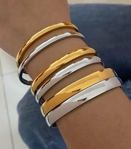 Stack of gold and silver minimalist stainless steel bracelets on model wrist