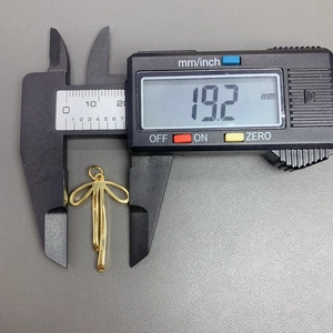Macro shot showing measurement of a gold bow pendant with zircon using digital calipers
