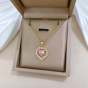 Detailed close-up of a golden heart pendant with a pink gemstone in a beige jewelry box