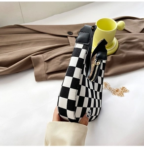Detail of checkered baguette bag with gold chain strap and black leather handle