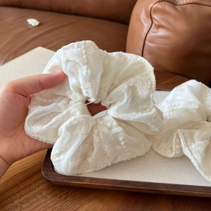 Close-up of elegant white lace scrunchie with floral embroidery on wooden tray