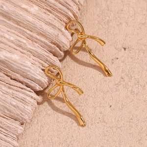 Close-up of gold bow earrings on a textured stone background with a minimalist design