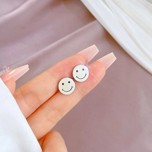 Detail view of silver smile face titanium steel stud earrings held by hand