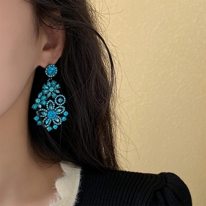 Close-up of peacock blue rhinestone floral drop earrings worn on a female model