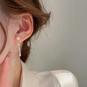 Close-up of elegant gold earrings with pearls and zircon tassels worn by a model