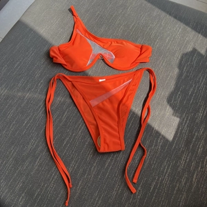 Detailed view of orange bikini top with asymmetric mesh panel and wire support