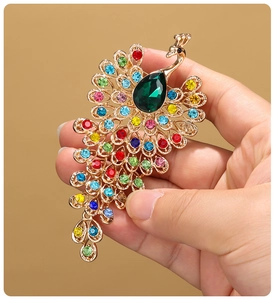 Macro shot of gold peacock brooch with colorful rhinestones and teardrop green gemstone