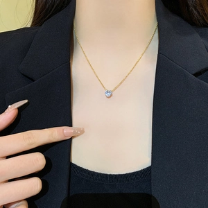 Close-up of heart-shaped crystal pendant on a gold chain necklace worn over a black blazer