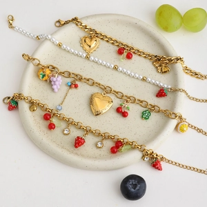 Detailed view of 18K gold plated stainless steel bracelets with fruit charms on a ceramic plate
