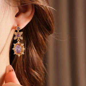 Close-up of vintage gold floral earrings with purple oval stones and white zircon on model