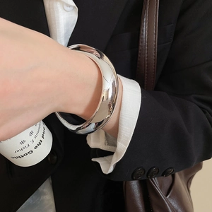 Close-up of polished silver geometric bangle worn with a chic black blazer and white shirt