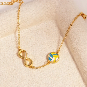 Detail eines 14k Gold Unendlichkeits-Armbands mit Volleyball-Emaille-Anhänger auf Samt