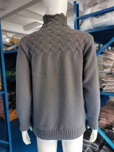 Detail of dark grey cable-knit texture and ribbed turtleneck on a long-sleeve sweater