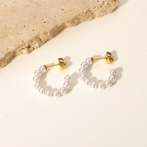 Detail of C-shaped pearl earrings with gold plating on a textured stone background