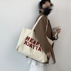 Detail of cream canvas tote bag featuring a bold red HEART ATTACK print and shoulder strap
