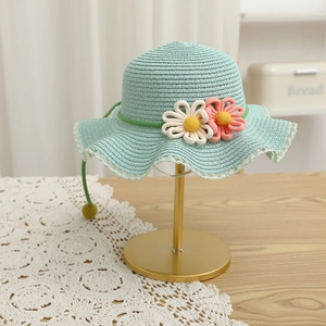 Detail of mint green straw hat featuring wavy brim and delicate handmade woven flowers