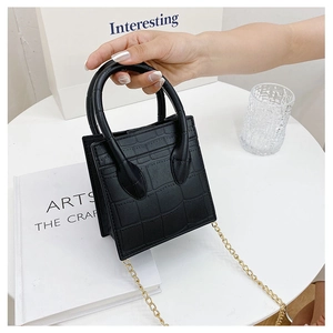 Detail of black crocodile texture mini bag with gold chain and top handle on table
