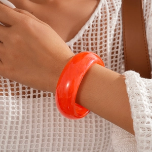 Detailed view of translucent orange resin bangle on wrist with knit sleeve background