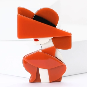 Detailed view of an orange acrylic silhouette brooch depicting a lady in a wide-brimmed hat