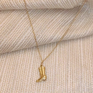Close-up of a vintage cowboy boot pendant with intricate Western embroidery on a gold chain