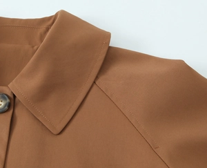 Macro detail of twill fabric collar and brown resin buttons on a cropped trench coat