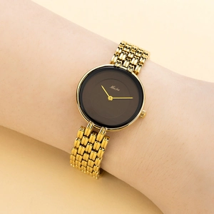 Close-up of golden quartz watch with black dial worn on wrist showing metal chain strap