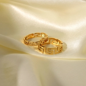 Golden stainless steel rings with Greek Key geometric cutouts on soft silk background