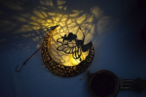 Solar moon wind chime with fairy silhouette casting dreamy light patterns on garden wall