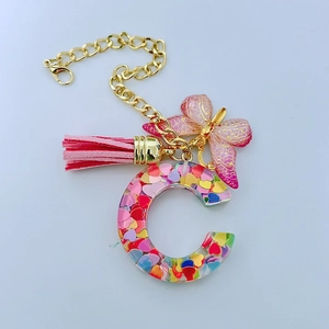 Detail of Letter C resin keychain with pink butterfly charm and suede tassel accessory