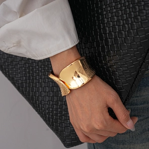 Detail of a wide gold metal cuff bracelet with hammered texture on a model's wrist