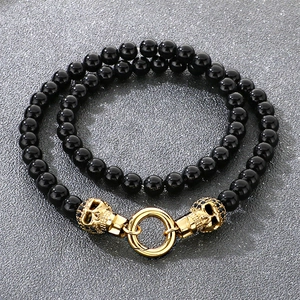 Détail d'un bracelet double couche en onyx noir avec crânes dorés sur fond de pierre grise