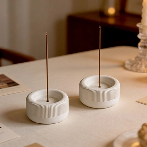 Two white ceramic incense holders with vertical stripe patterns on a cozy wooden table